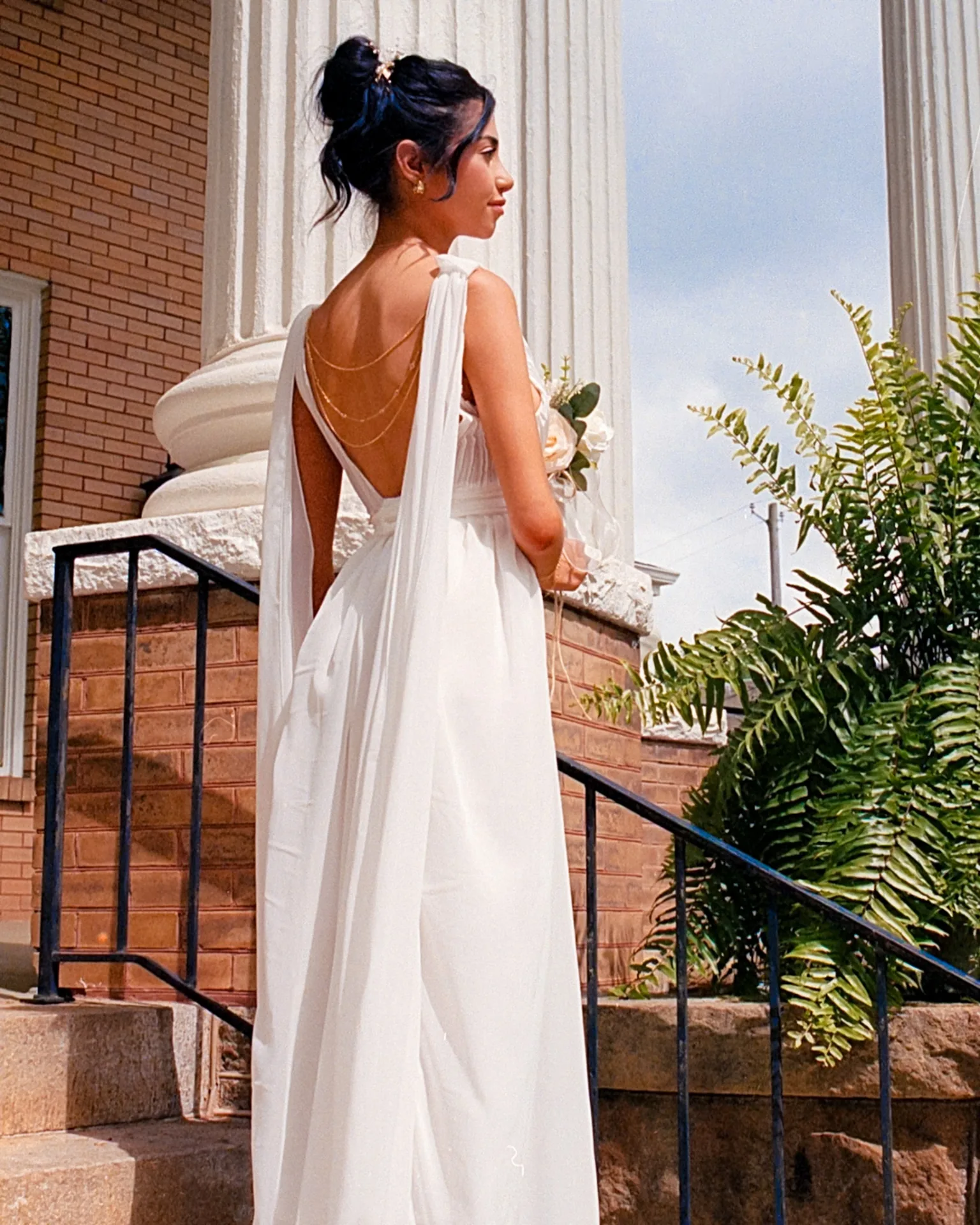 Bride in a backless dress photographed from behind near white columns