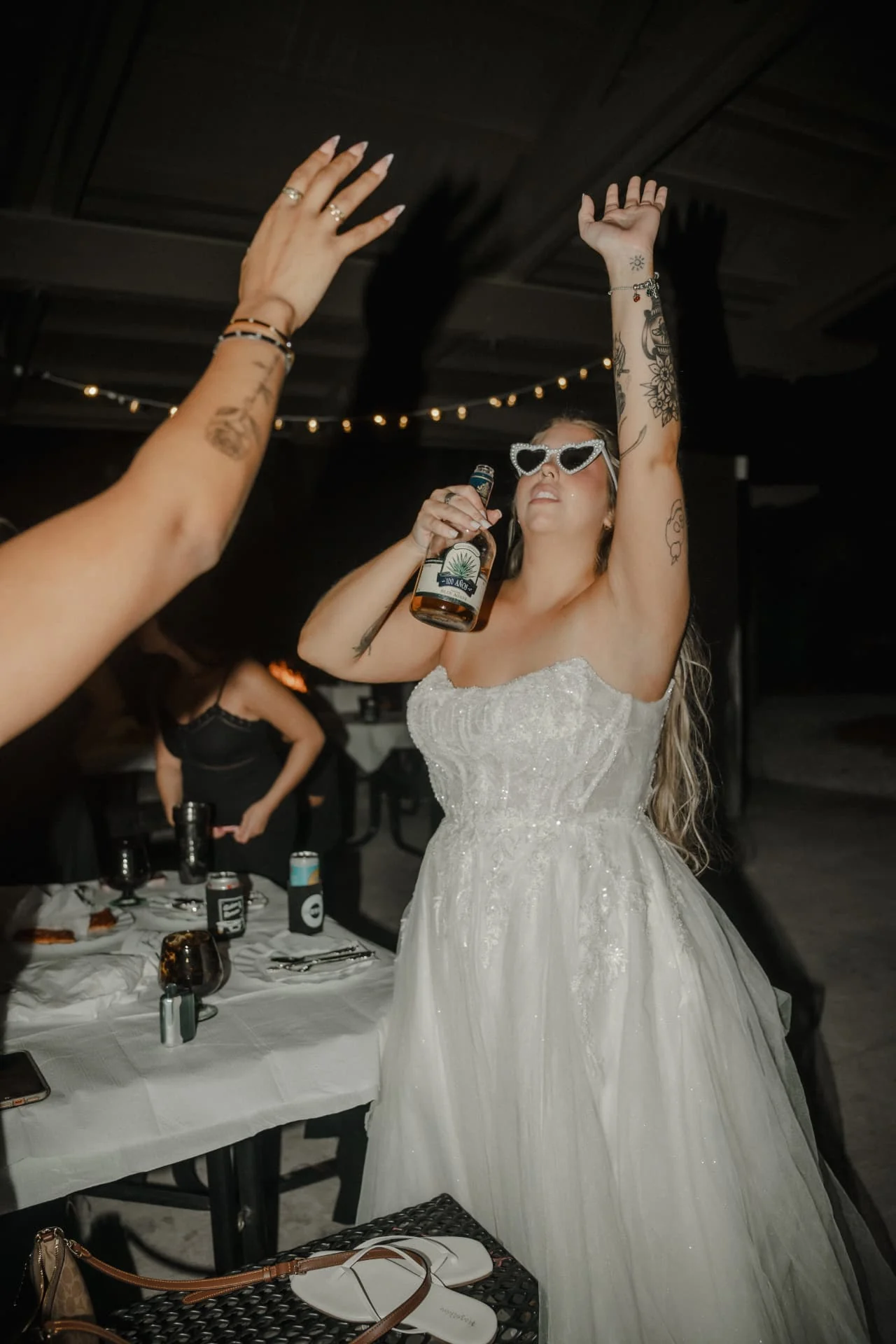 Bride raising her arm and celebrating in heart-shaped sunglasses at the wedding reception
