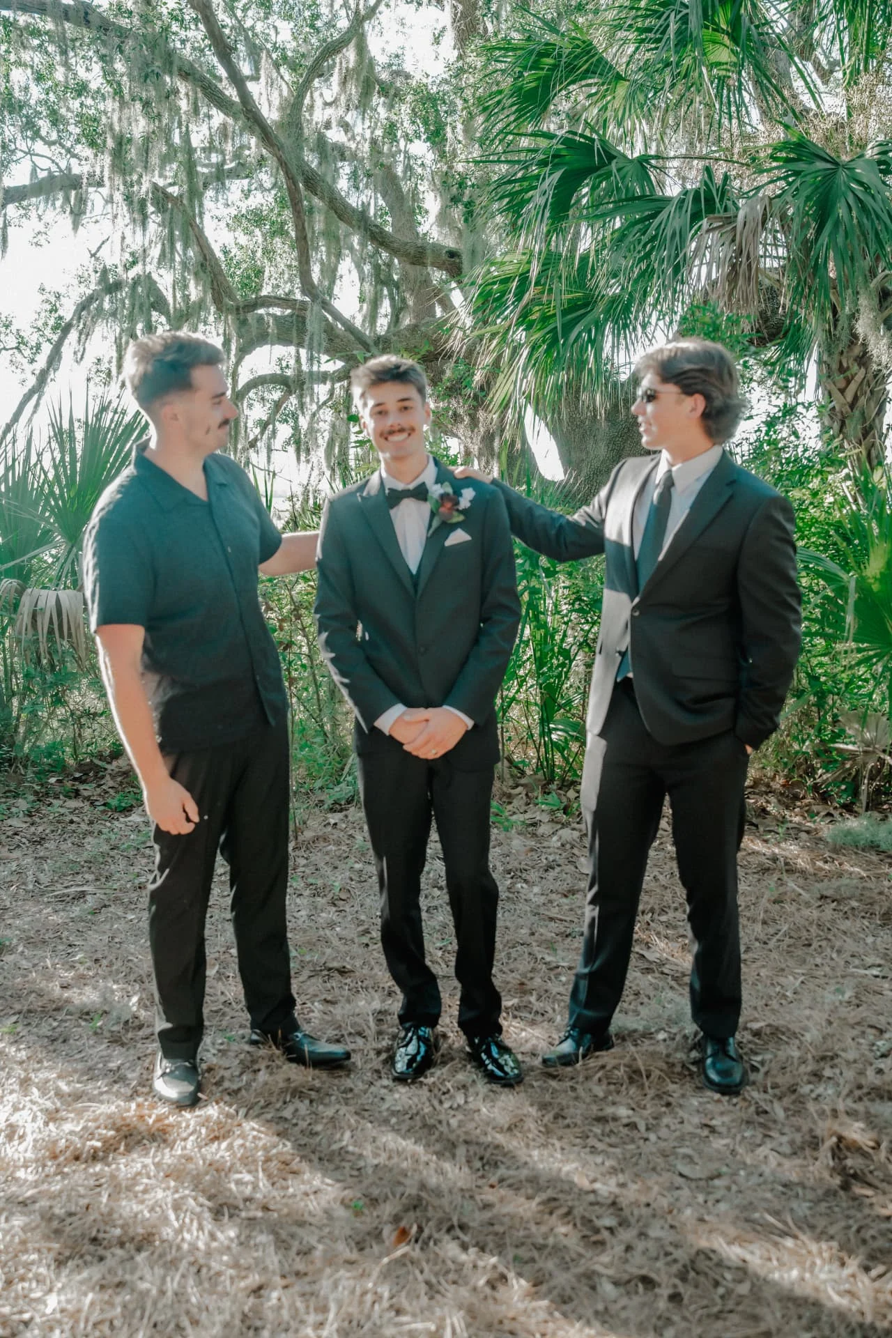 Groom laughing with his groomsmen beneath the moss-draped oaks