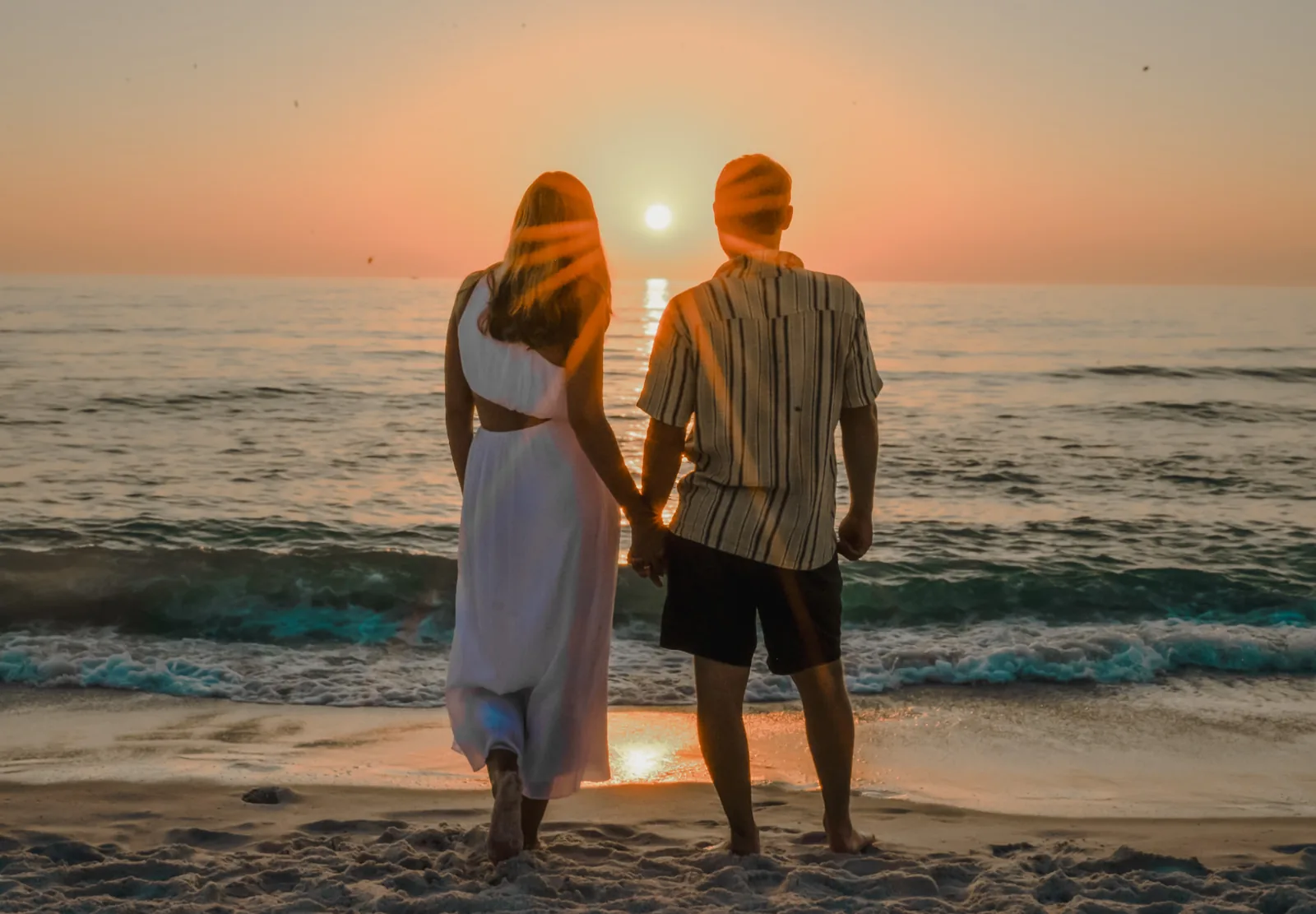 Engaged couple holding hands watching the sunset over the ocean