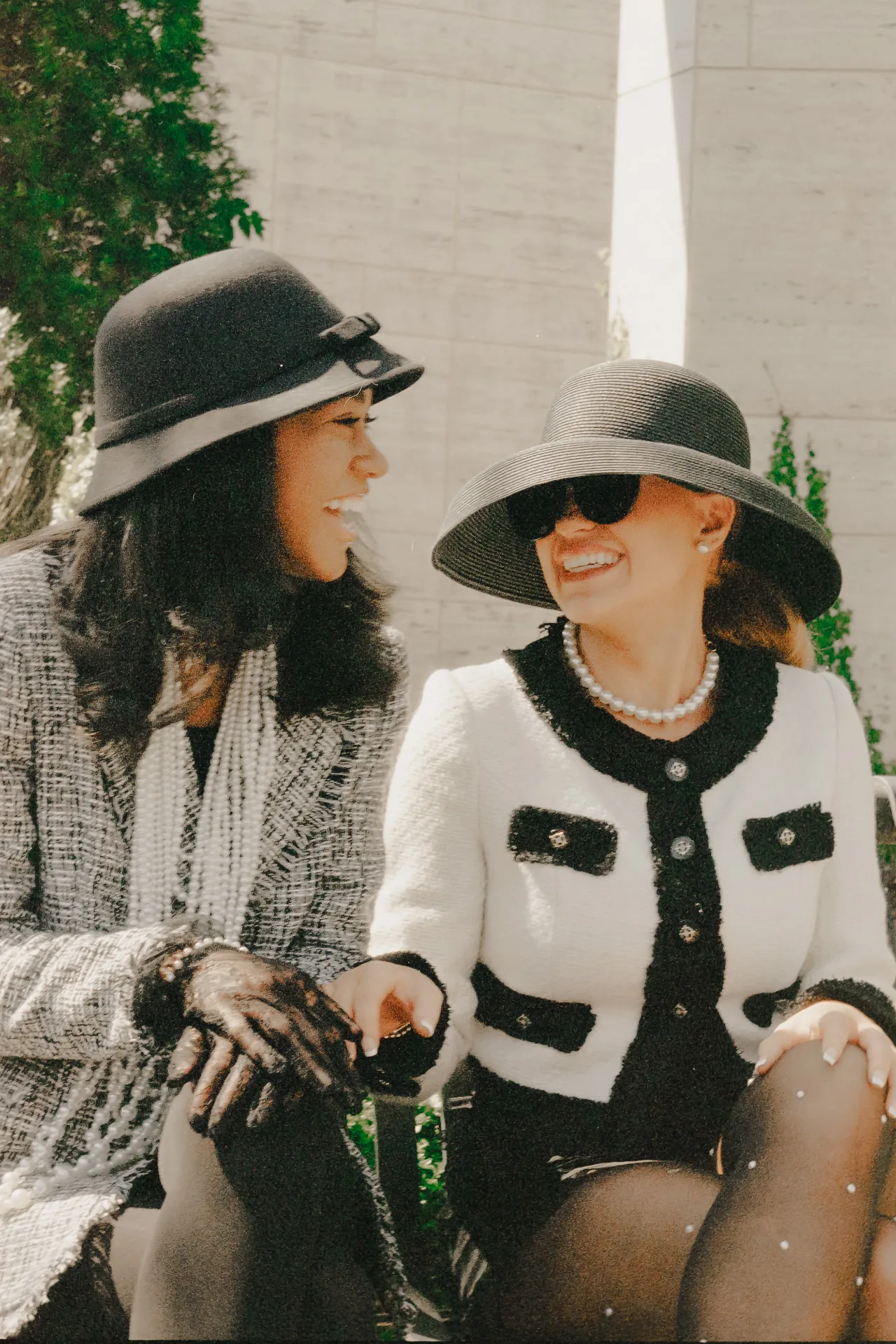 Two women in tweed and wide-brim hats with pearls laughing together on film