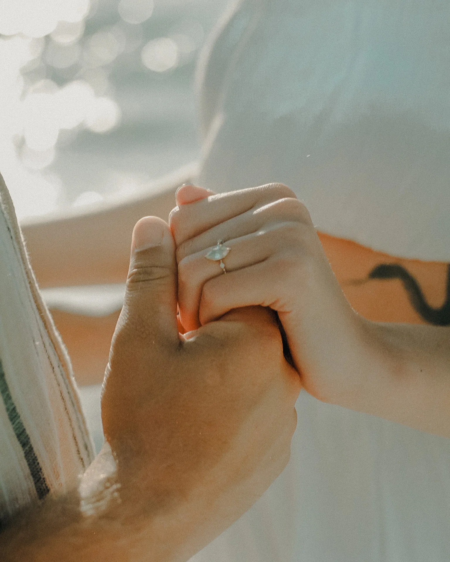 Two hands reaching toward each other with engagement and wedding rings above the surf