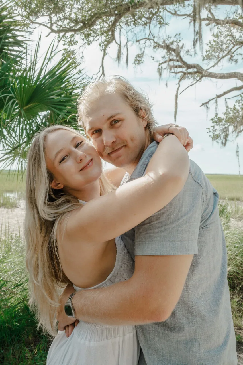 Engaged couple embracing under a palmetto tree beside a coastal marsh