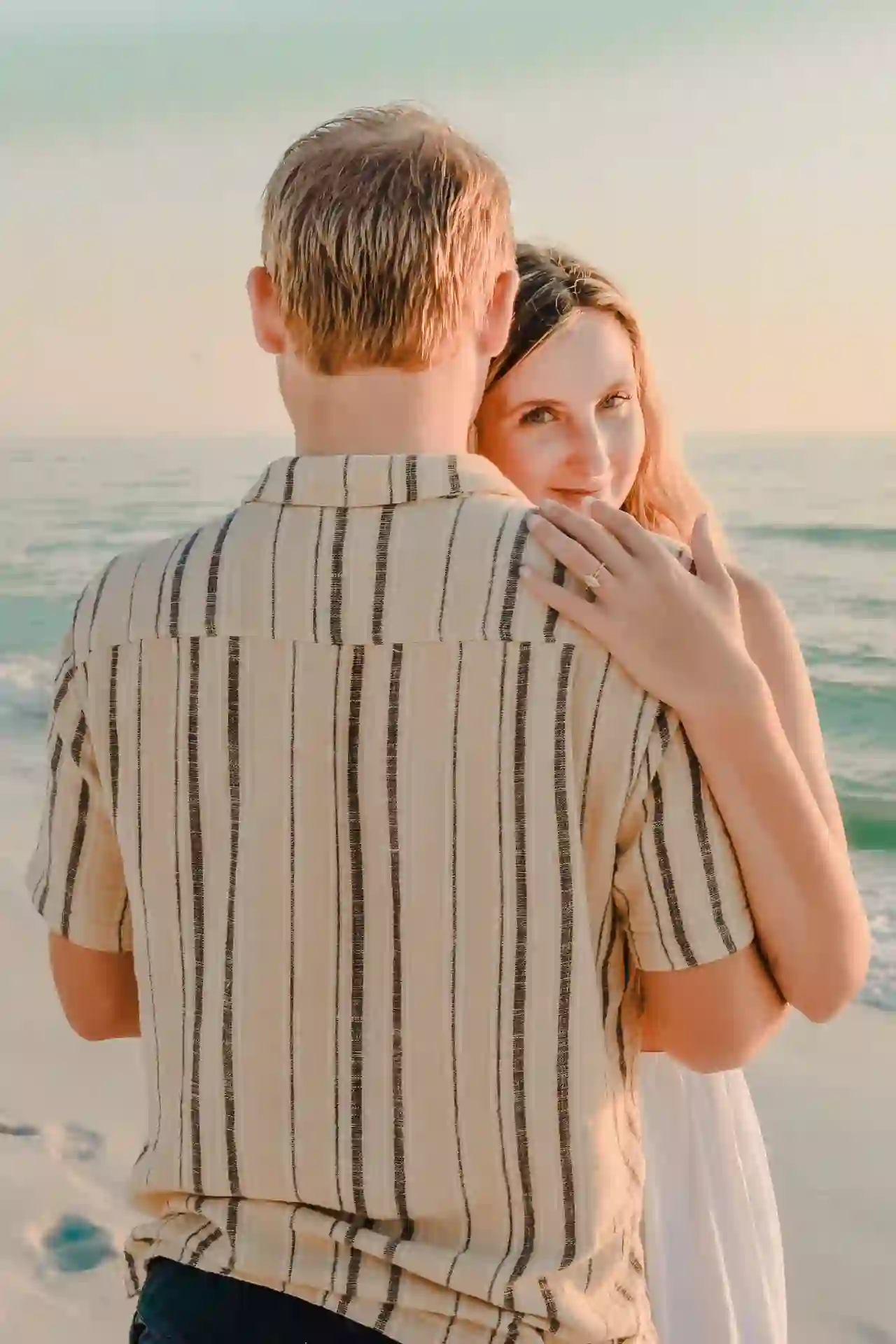 Bride-to-be resting on her fiance's shoulder at the beach with her ring showing