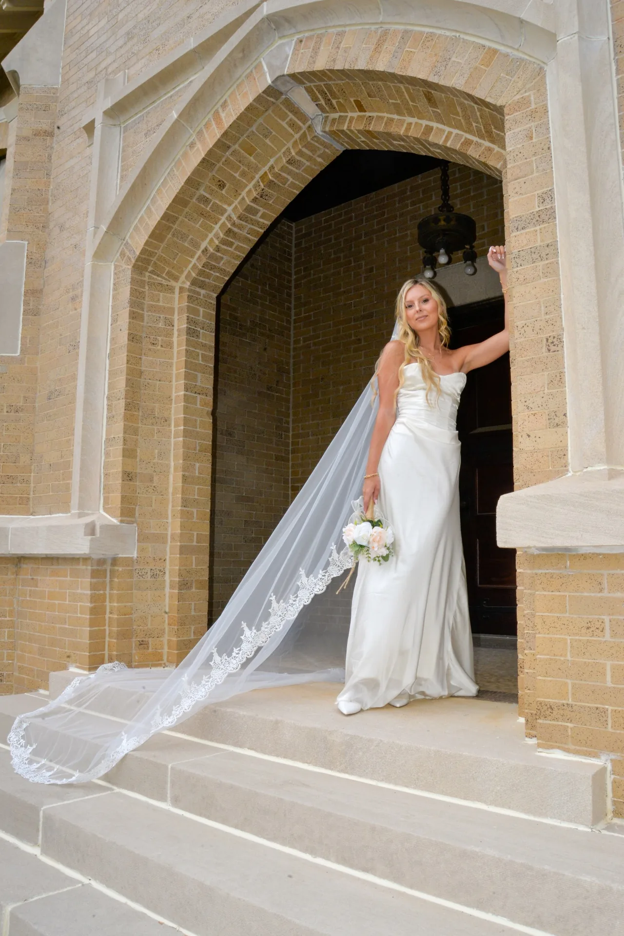 Bride beneath an arch with her veil flowing in a digital wedding portrait