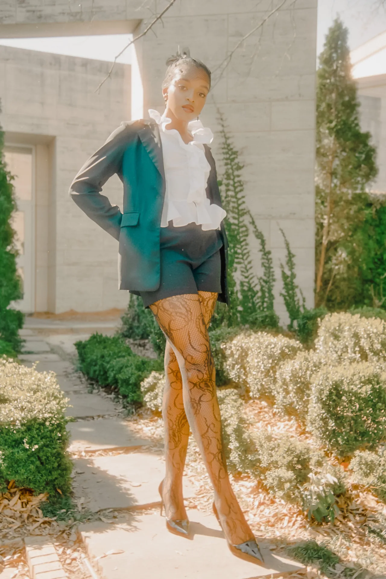 Editorial fashion portrait in a tailored suit and ruffled blouse in a sunlit garden on CineStill 400D film