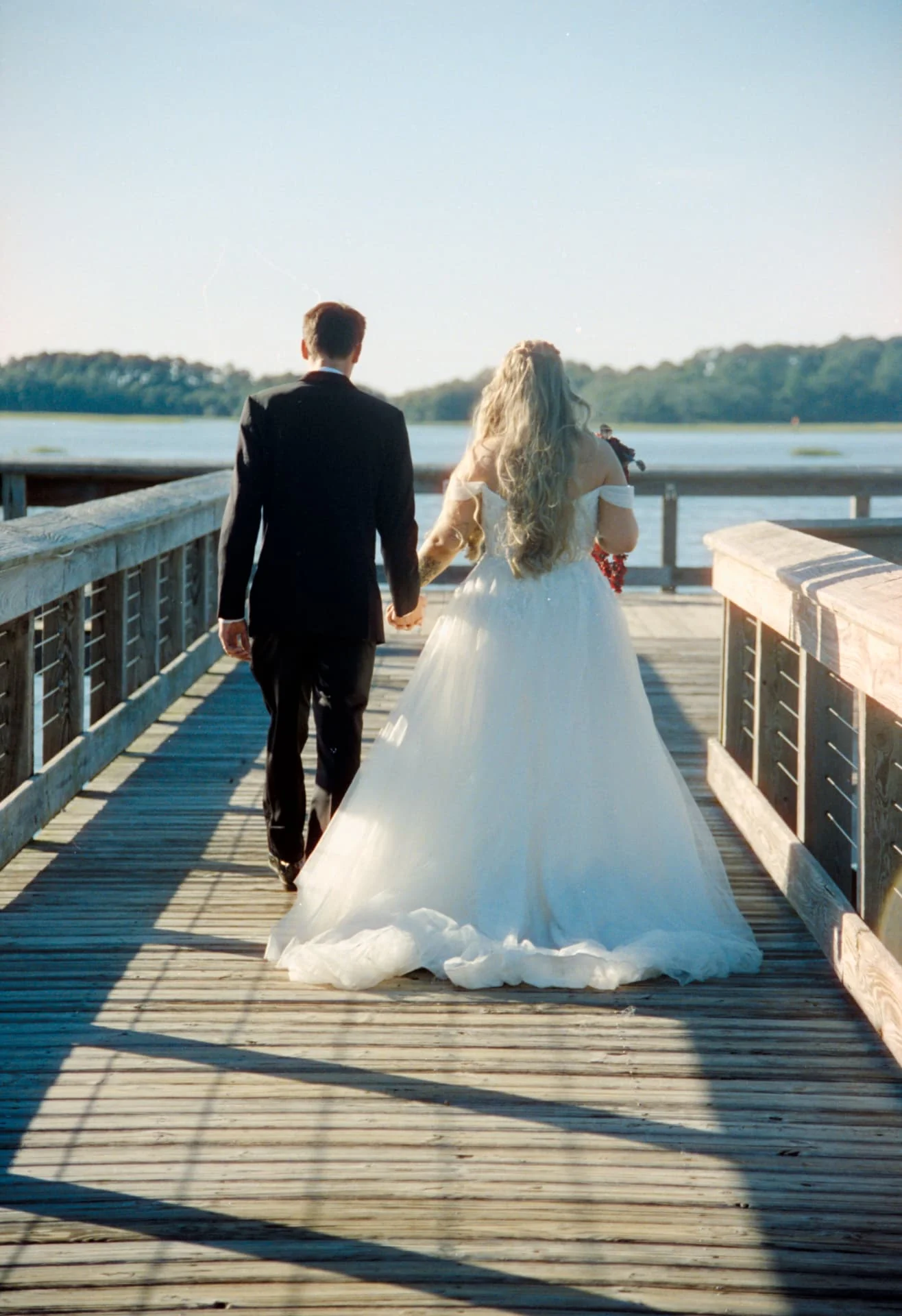 Newlyweds walking hand in hand down a sunlit dock on CineStill 400D wedding film