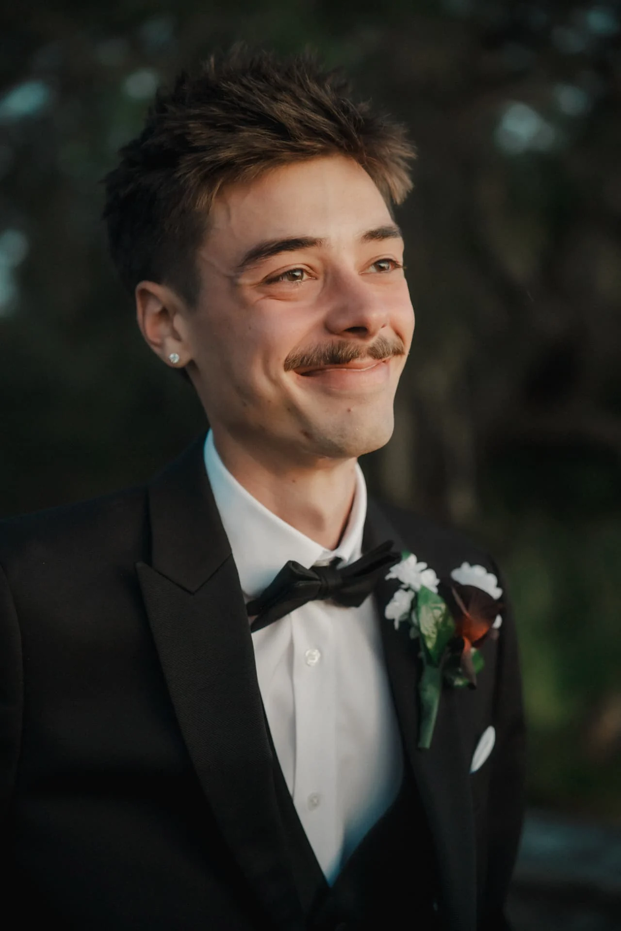 Candid portrait of the groom in a black tuxedo beneath the trees