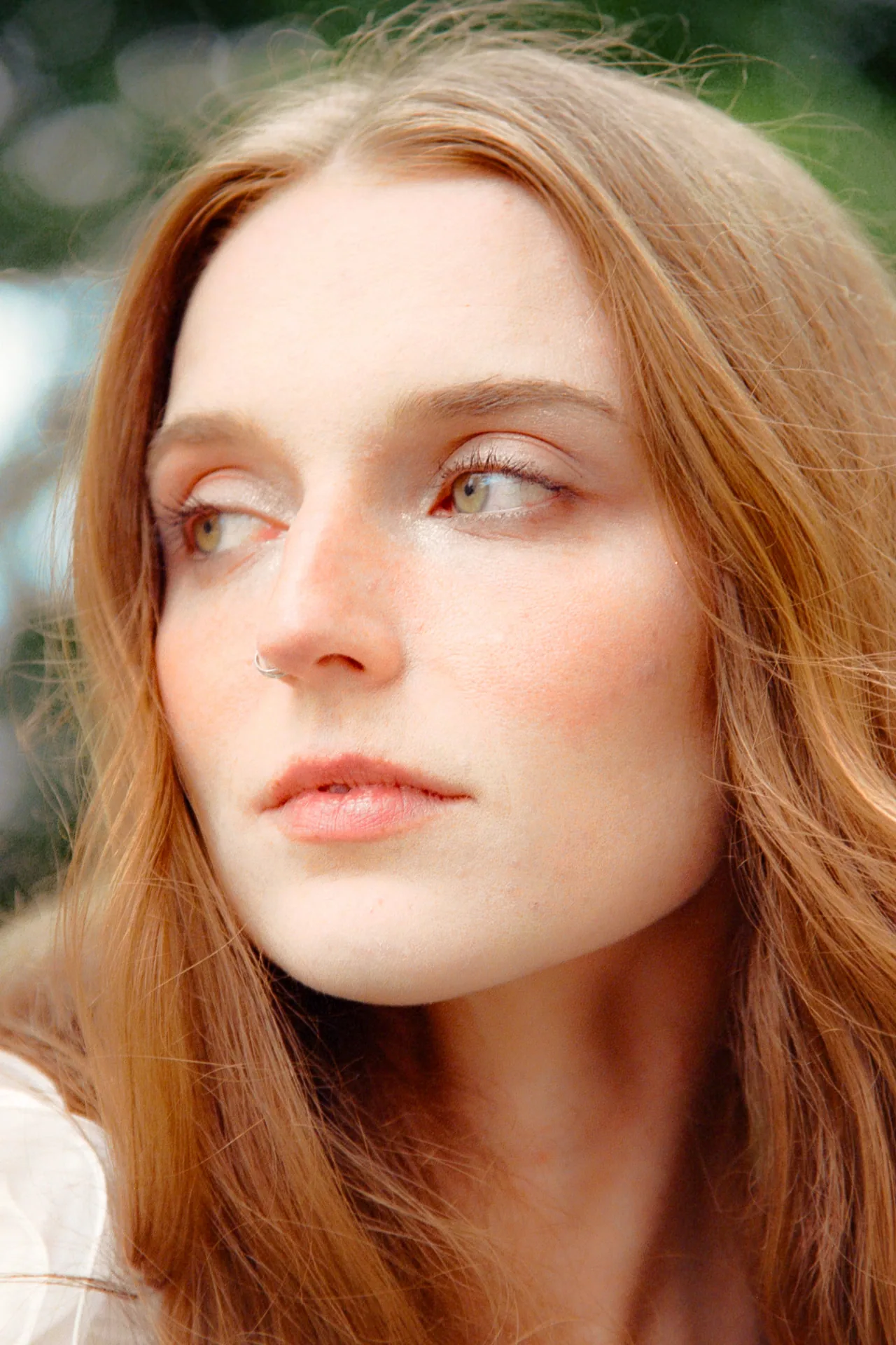 Close portrait of a red-haired bride looking off camera against soft green bokeh on Portra 400 film