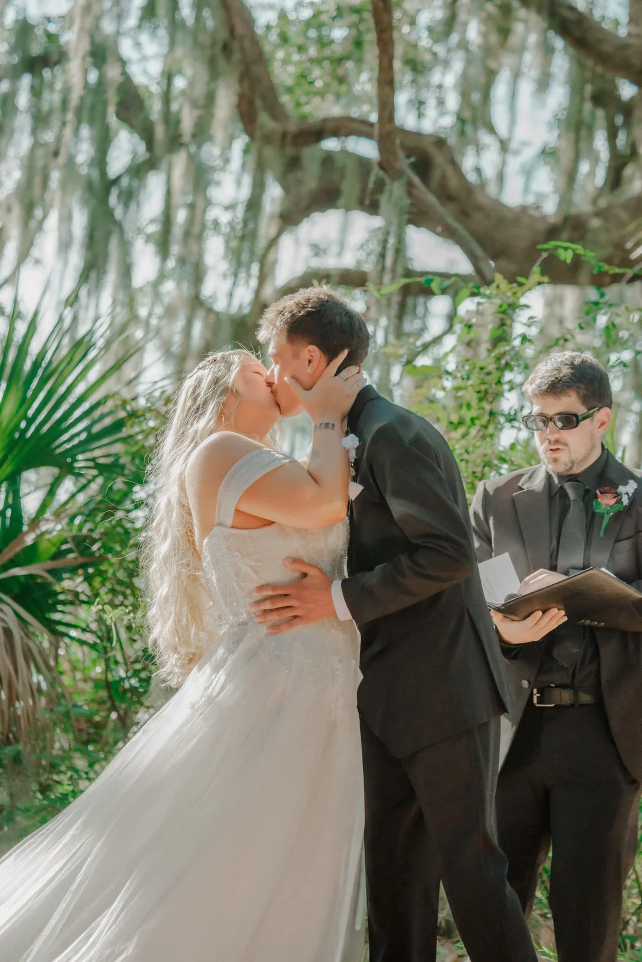 Bride and groom sharing their first kiss beneath moss-draped oaks at their ceremony
