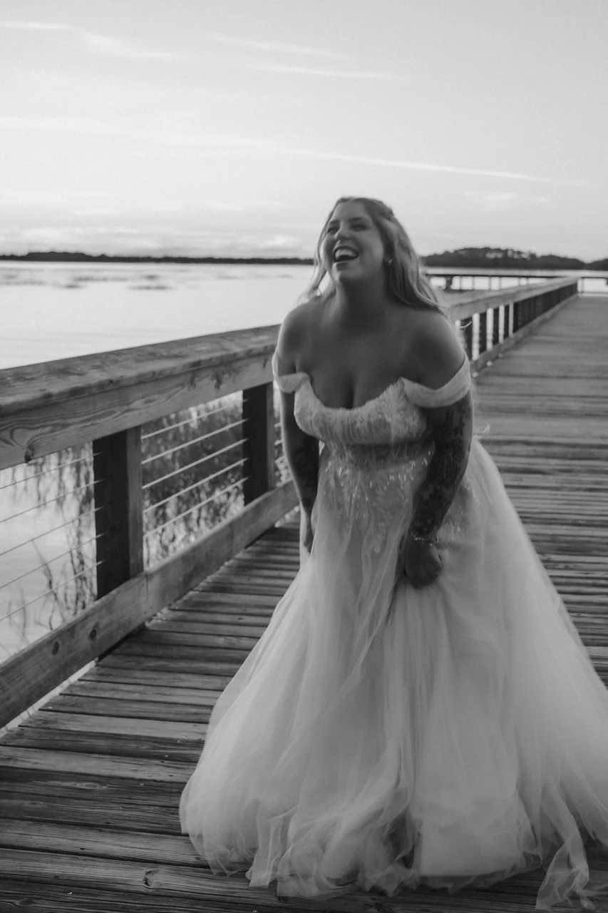 Black-and-white portrait of the bride laughing on a wooden dock at dusk