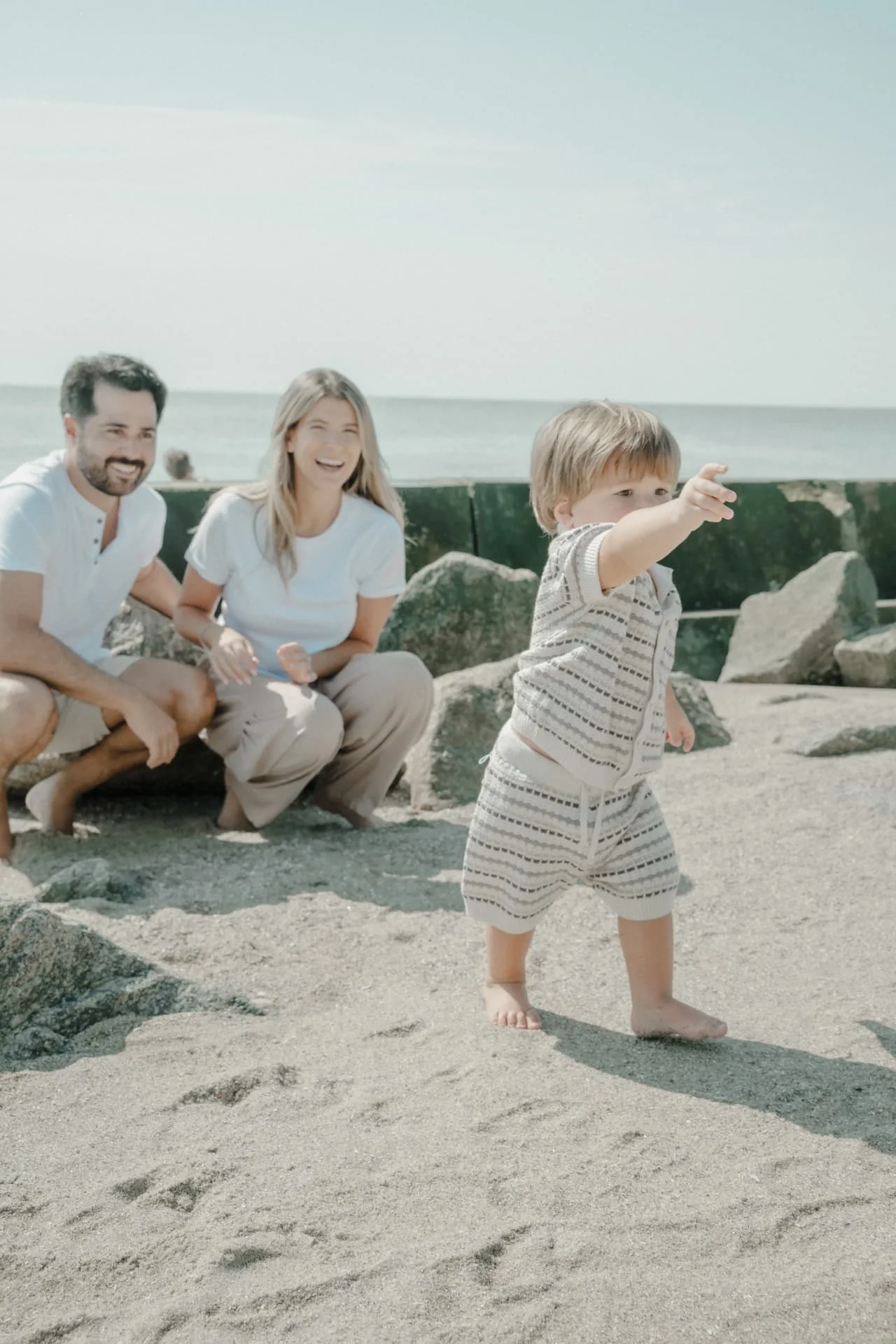 Young child walking on the beach with parents smiling nearby