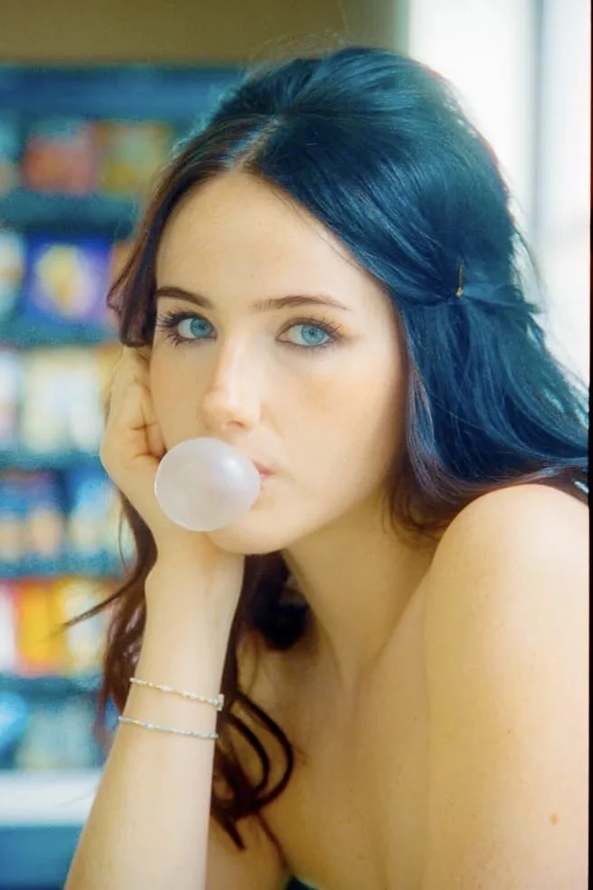 Close editorial portrait blowing bubblegum with vivid blue CineStill color