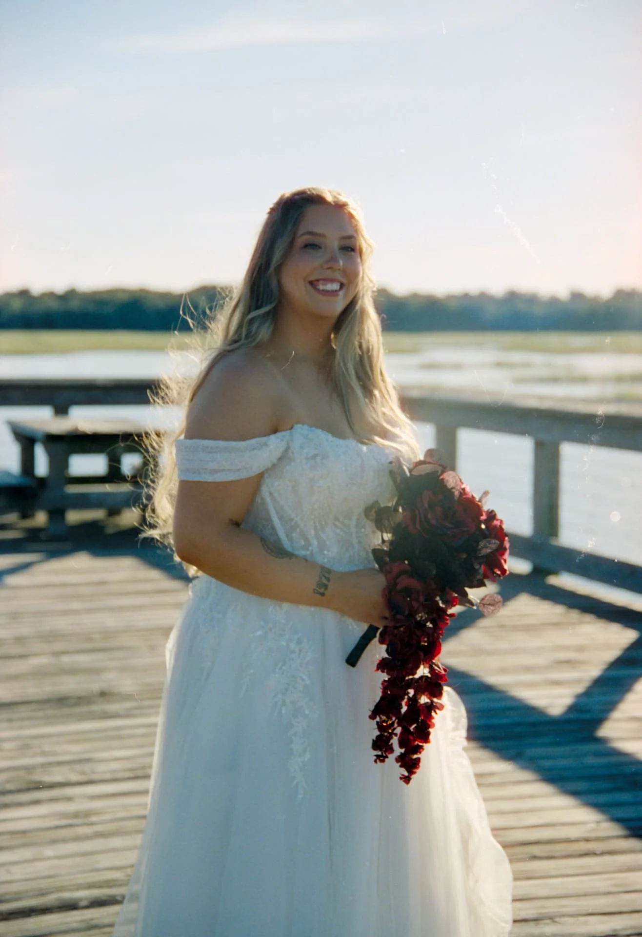 Bride holding a burgundy bouquet on a waterfront dock, photographed on CineStill 400D wedding film