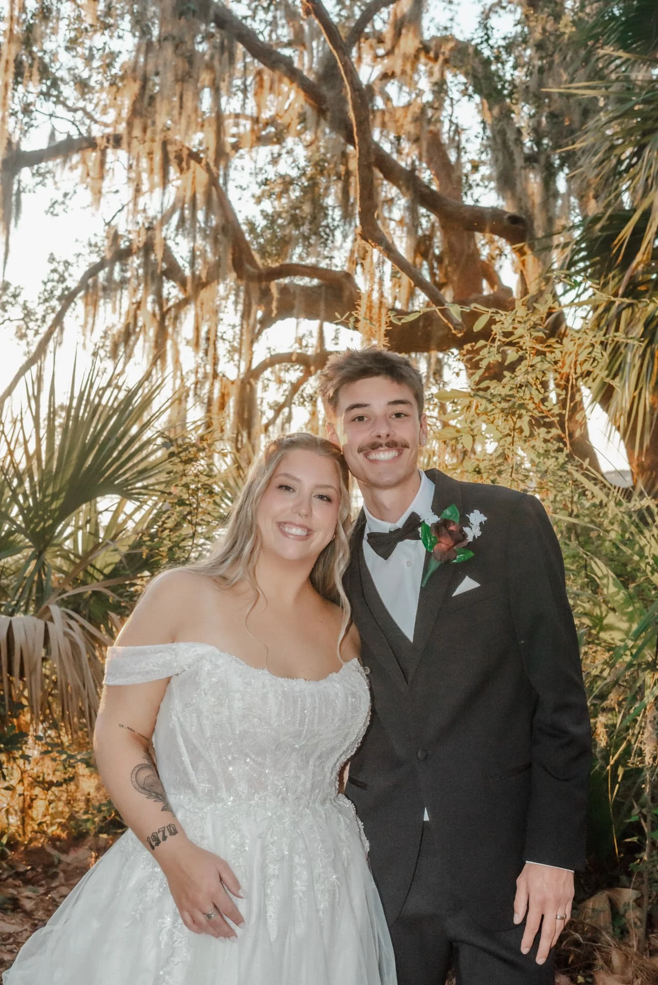 Bride and groom smiling beneath sunlit Spanish moss and palms