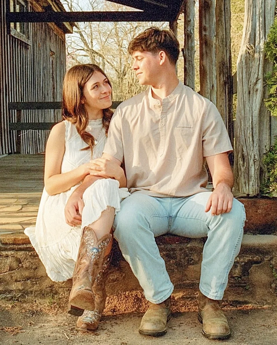 Engaged couple seated together on rustic stone steps in warm afternoon light