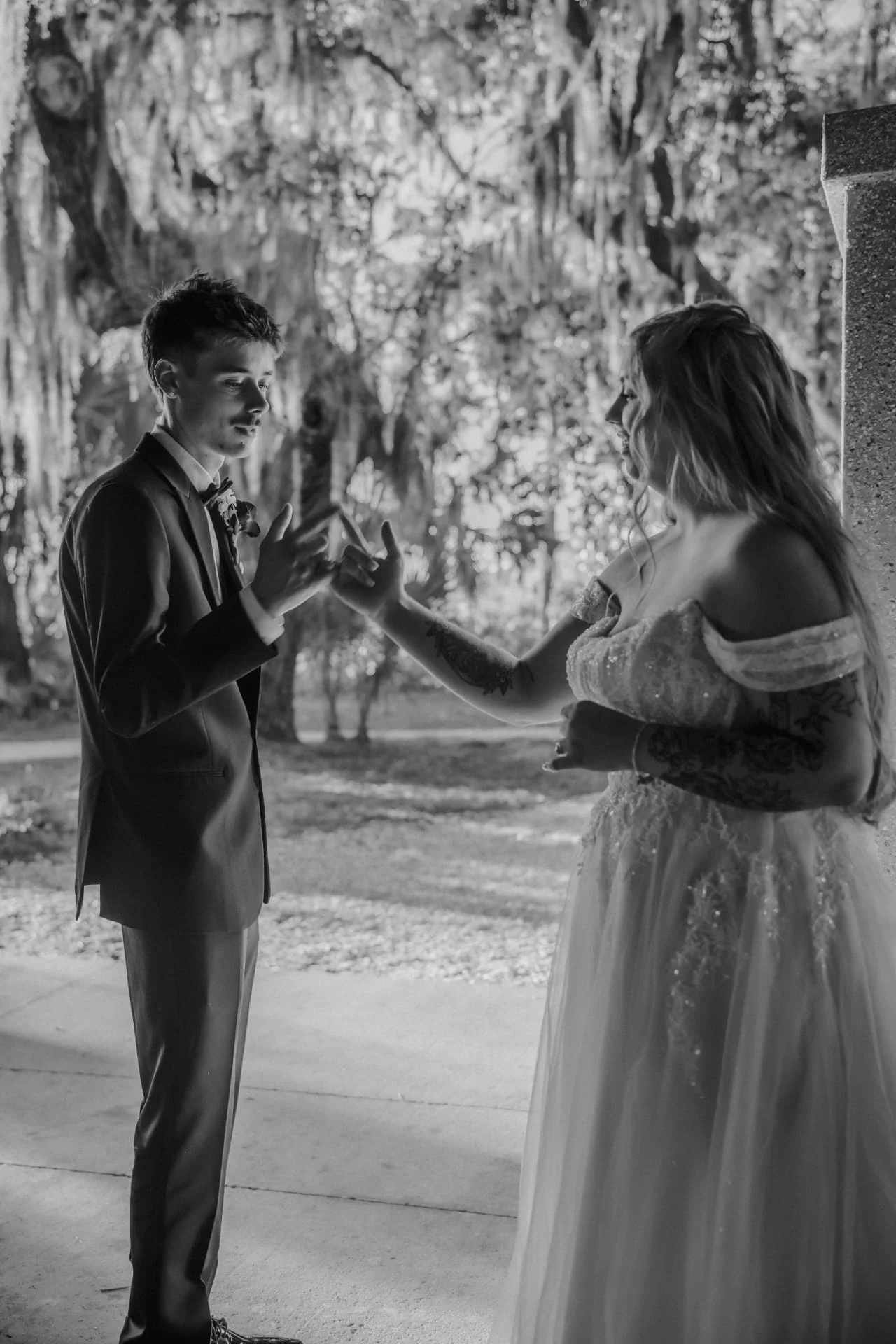 Black-and-white candid of the groom holding the laughing bride's hand beneath Spanish moss