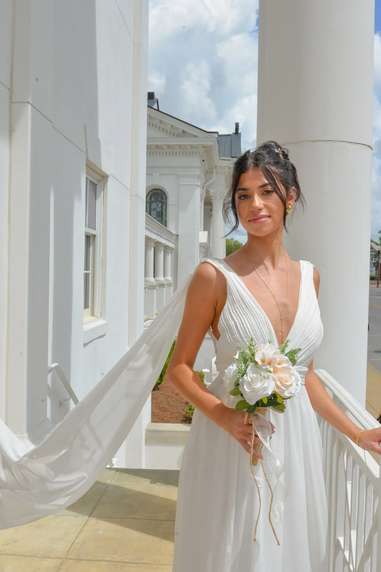 Bride beside white columns with her veil flowing in a digital portrait
