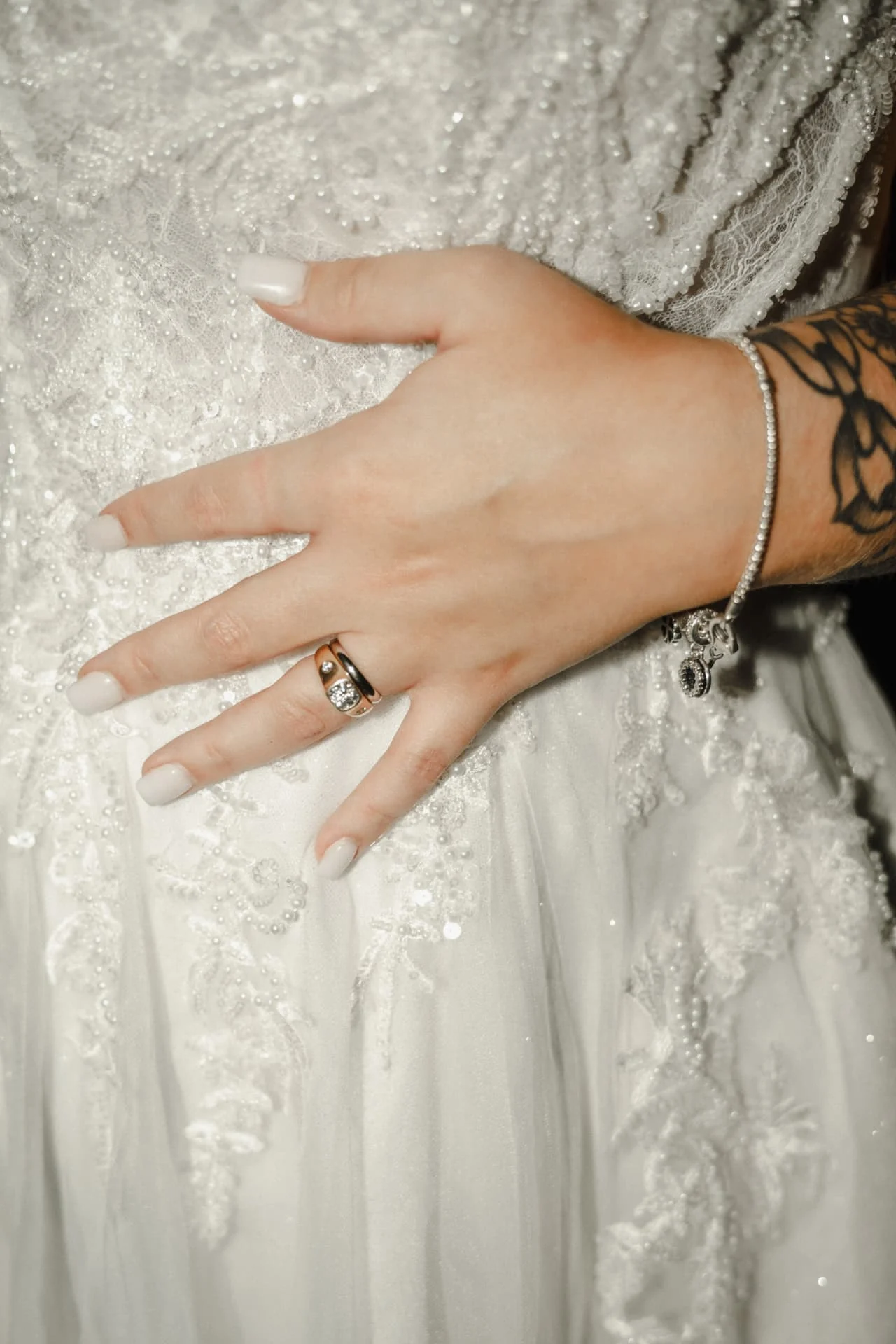 Close-up of the bride’s wedding rings and bracelet against her beaded gown