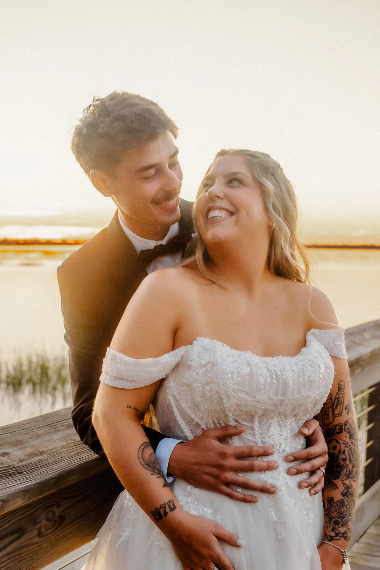 Groom embracing the bride beside the water at golden hour