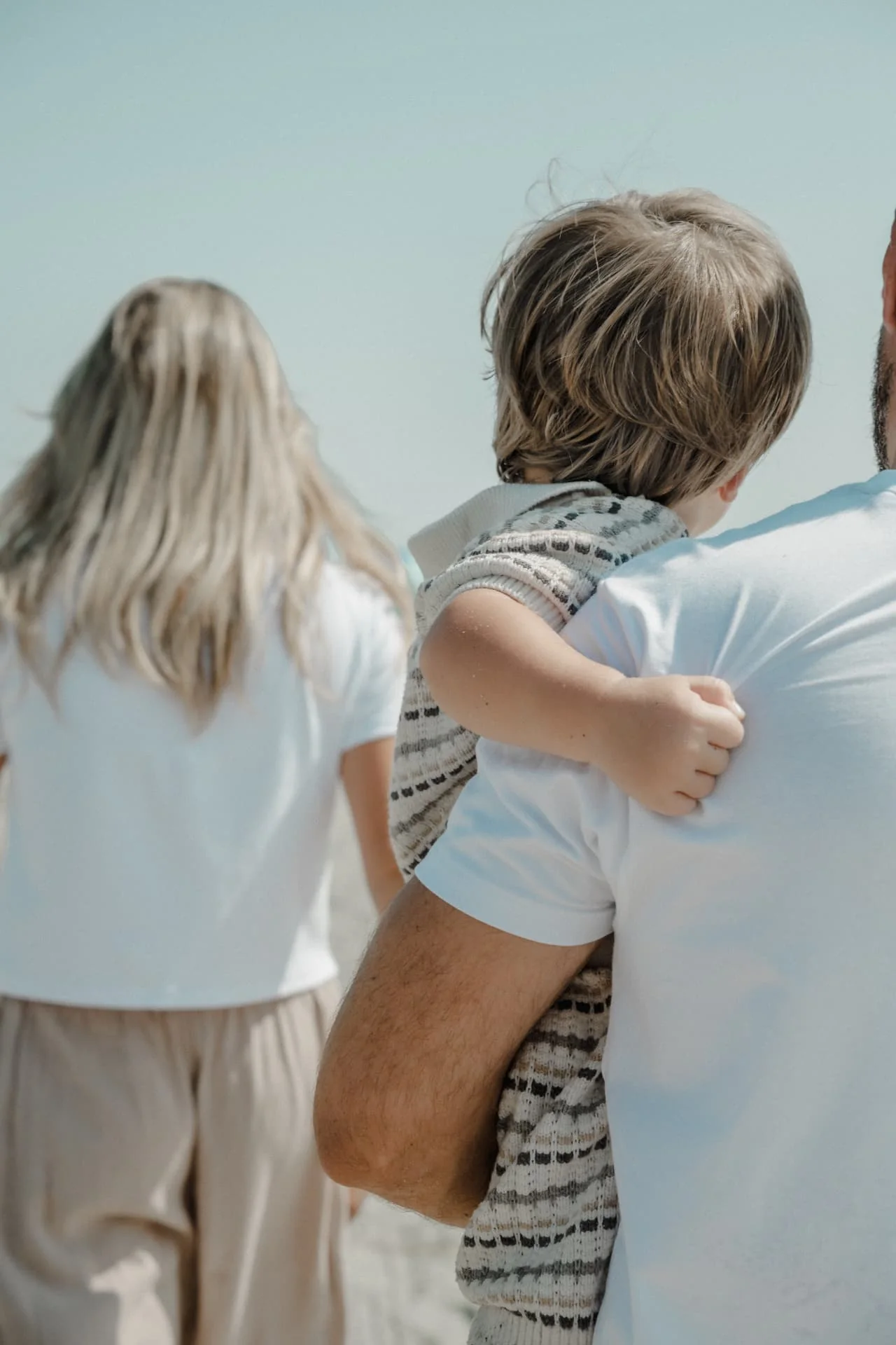 Father carrying his young child while the family walks along the beach