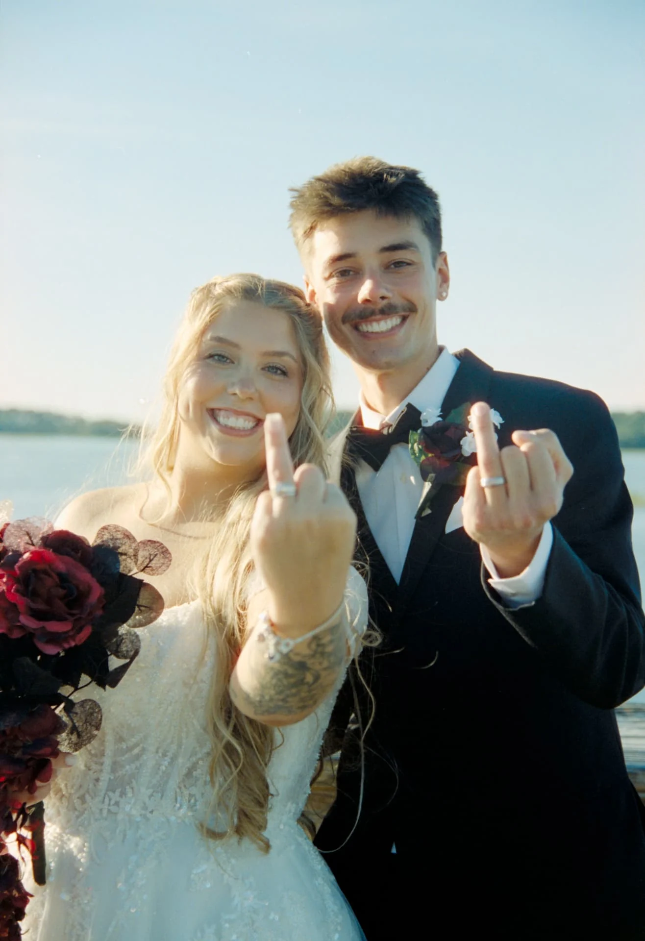 Newlyweds playfully showing their wedding rings beside the water on CineStill 400D film