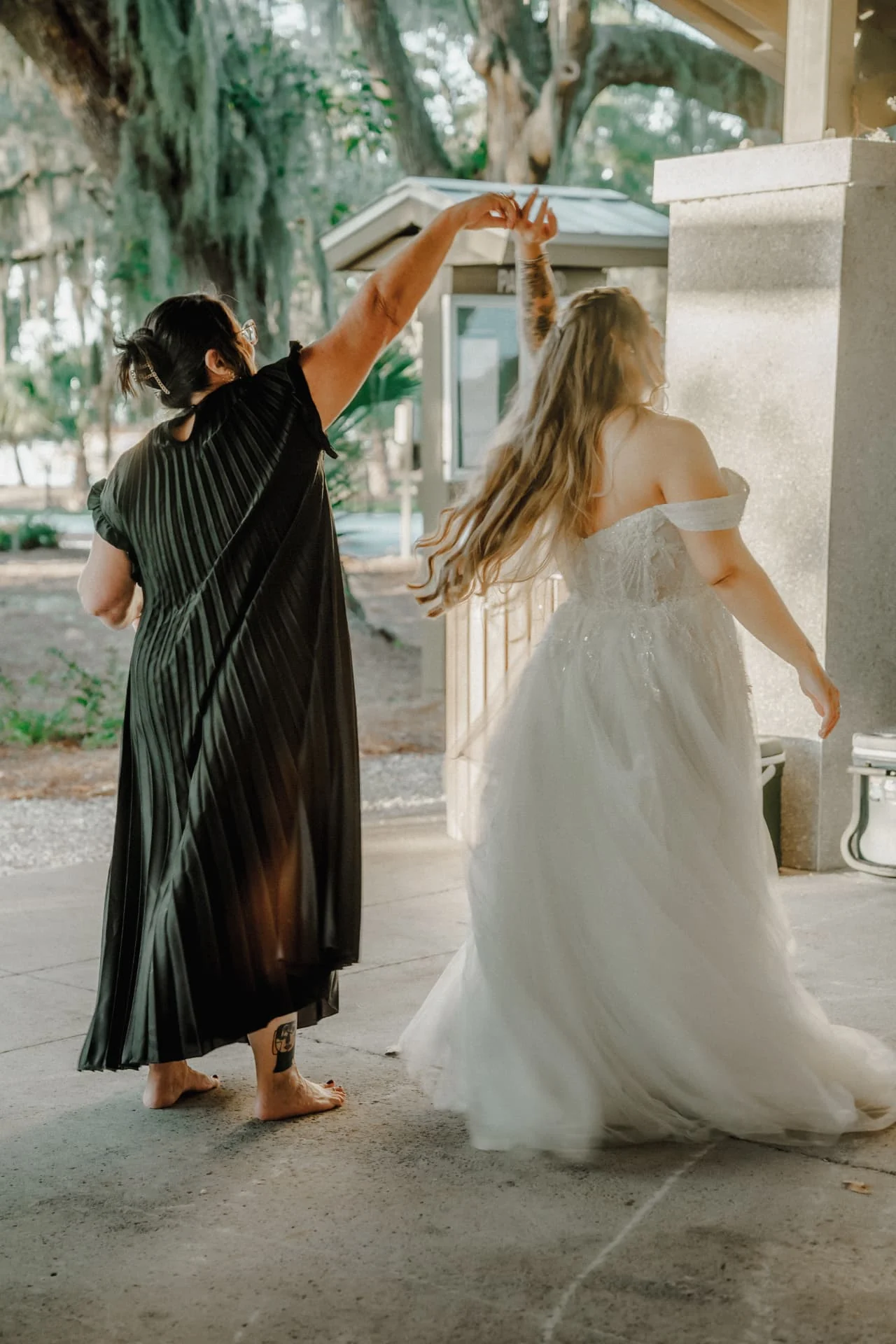 Bride twirling and laughing with a friend beneath the pavilion columns