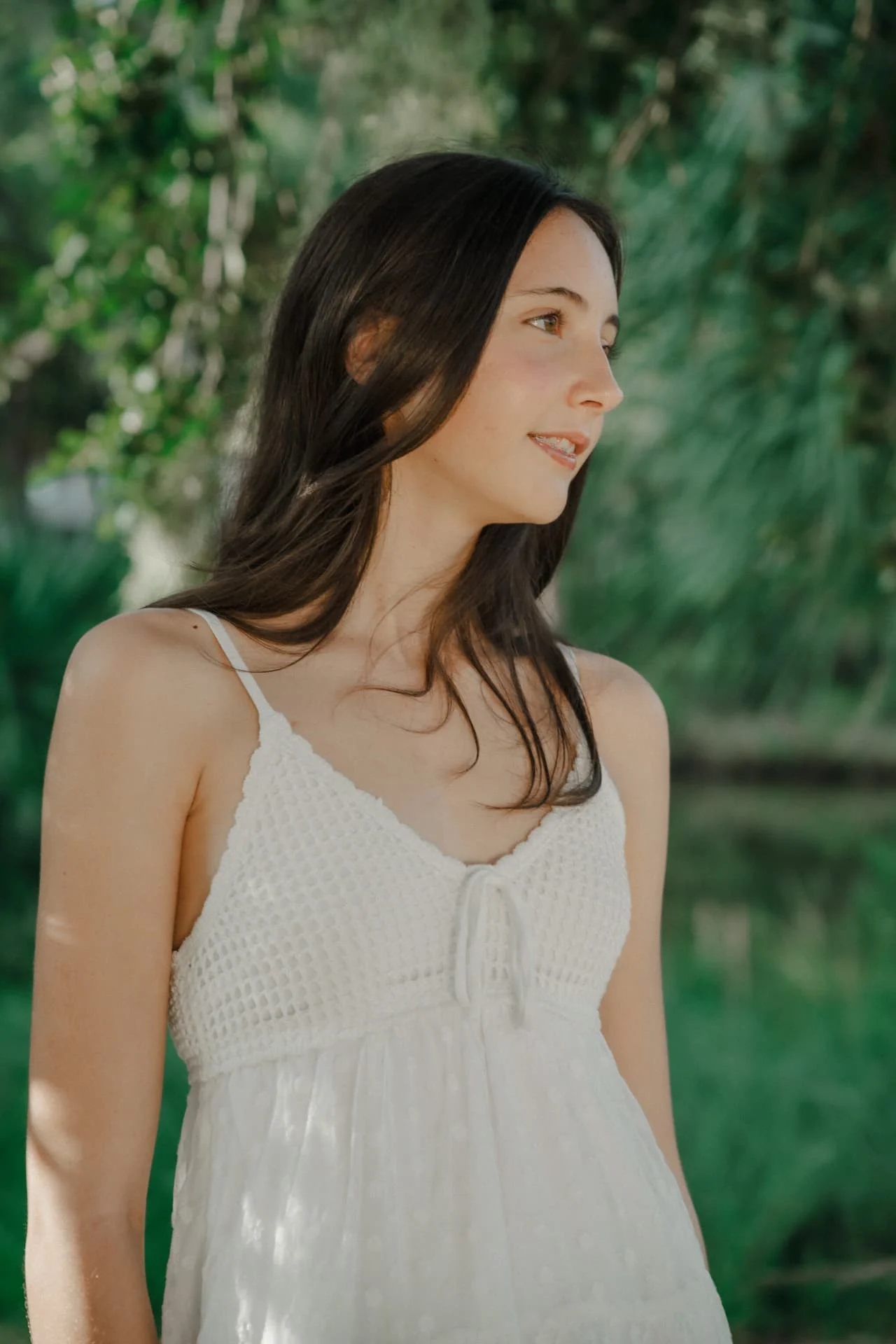 Portrait of a sister in a white crochet dress looking over her shoulder among the trees