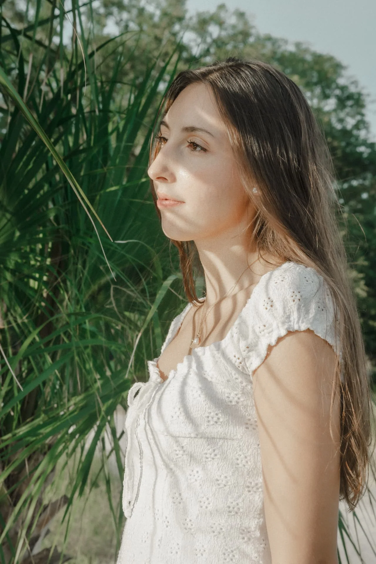 Sunlit portrait of one of two sisters in a white dress beside palmetto leaves