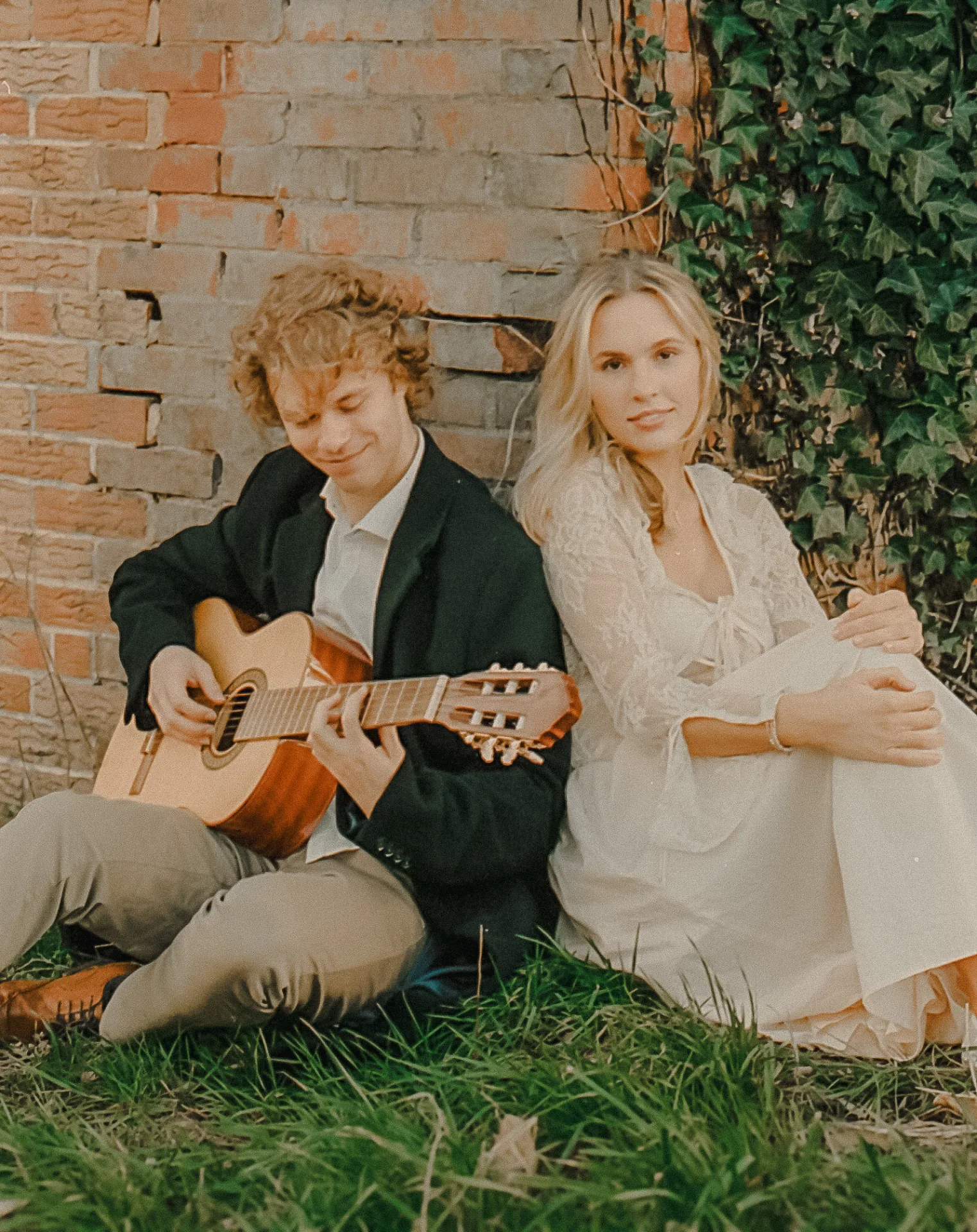 Couple with a guitar seated against an ivy brick wall on Portra 400 film