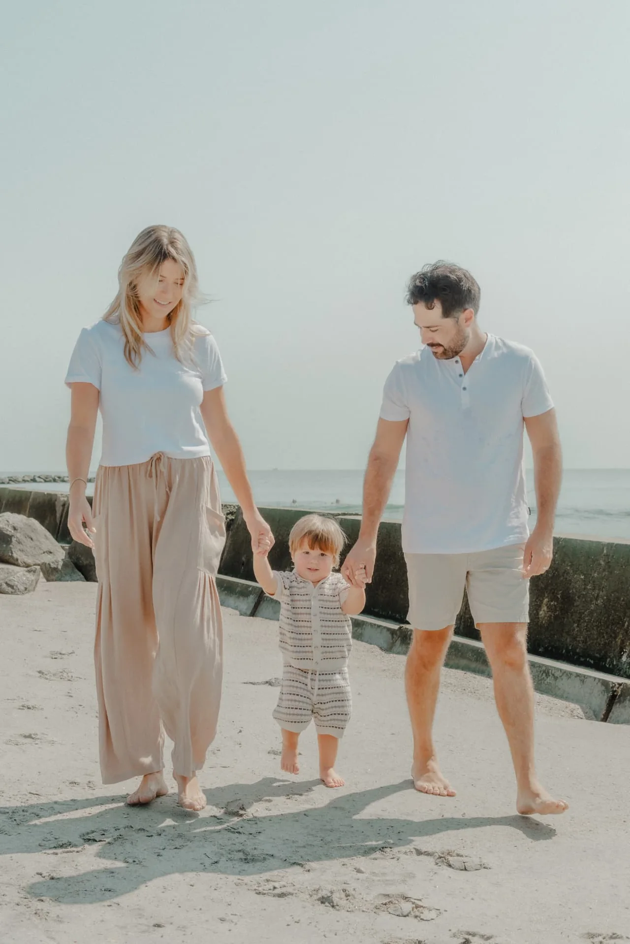 Parents walking hand in hand with their young child on the beach