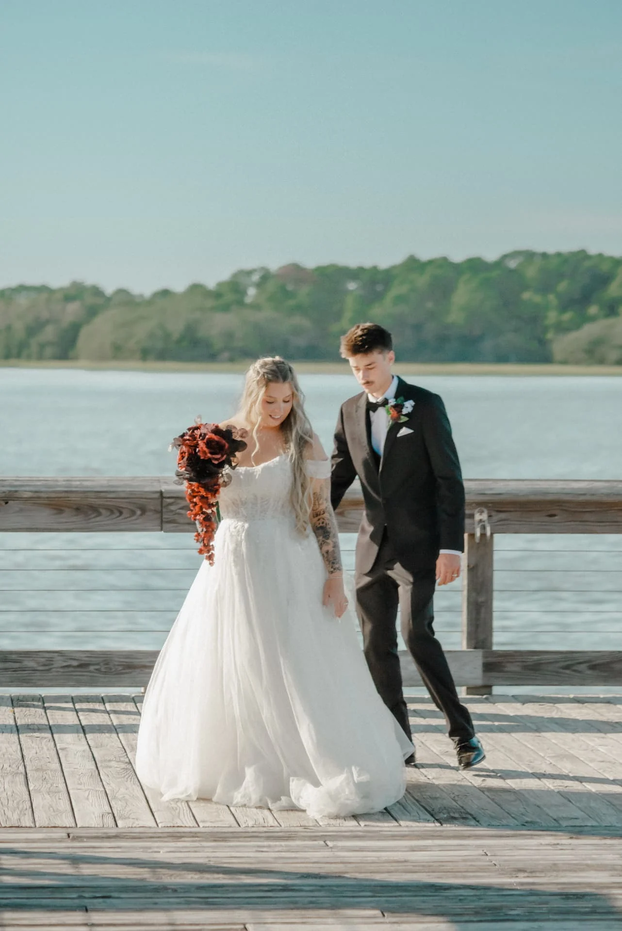 Newlyweds walking together across a sunlit waterfront dock